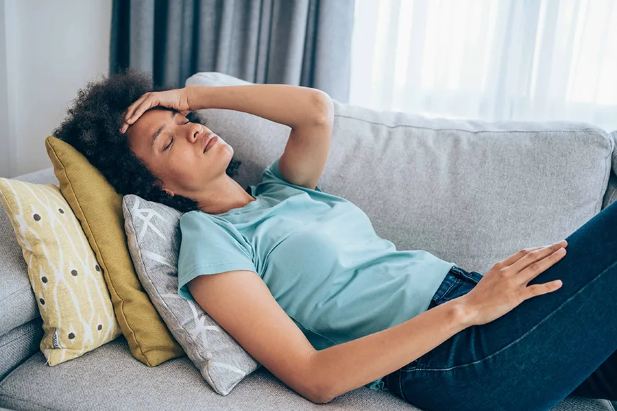 Person resting on a couch with signs of headache or exhaustion, illustrating common illness symptoms